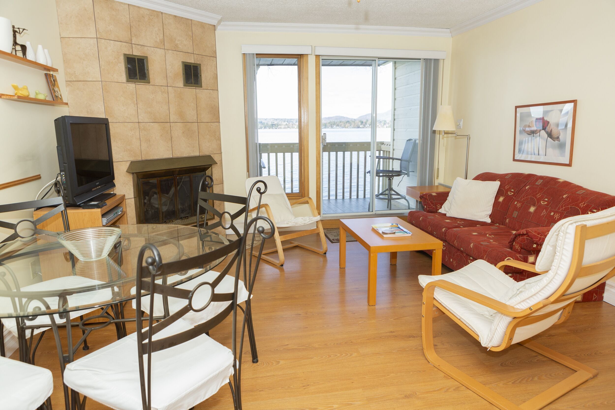 A living room with a fireplace, a glass table, a red sofa, and a balcony with a view.