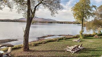 A lakeside view with lounge chairs and a picnic table, surrounded by trees and a mountain in the background.
