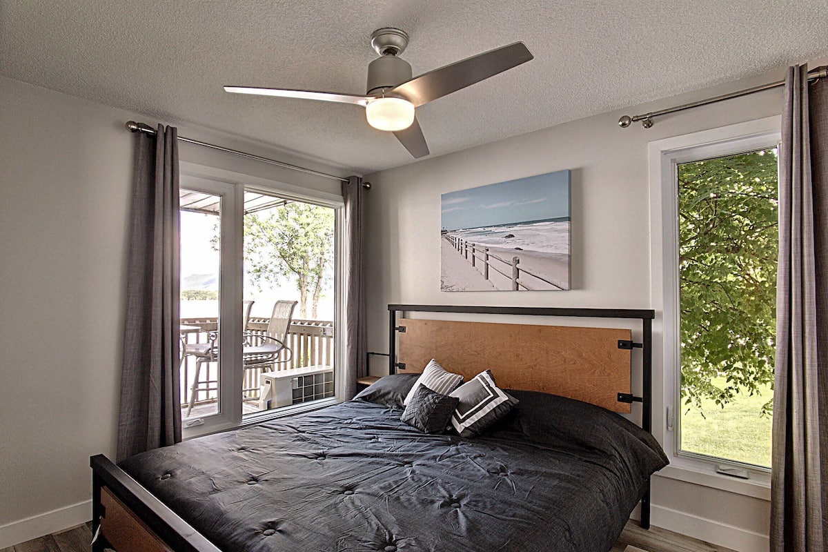 Une chambre à coucher avec un lit, un ventilateur de plafond, une fenêtre avec des rideaux et une vue sur l’extérieur.