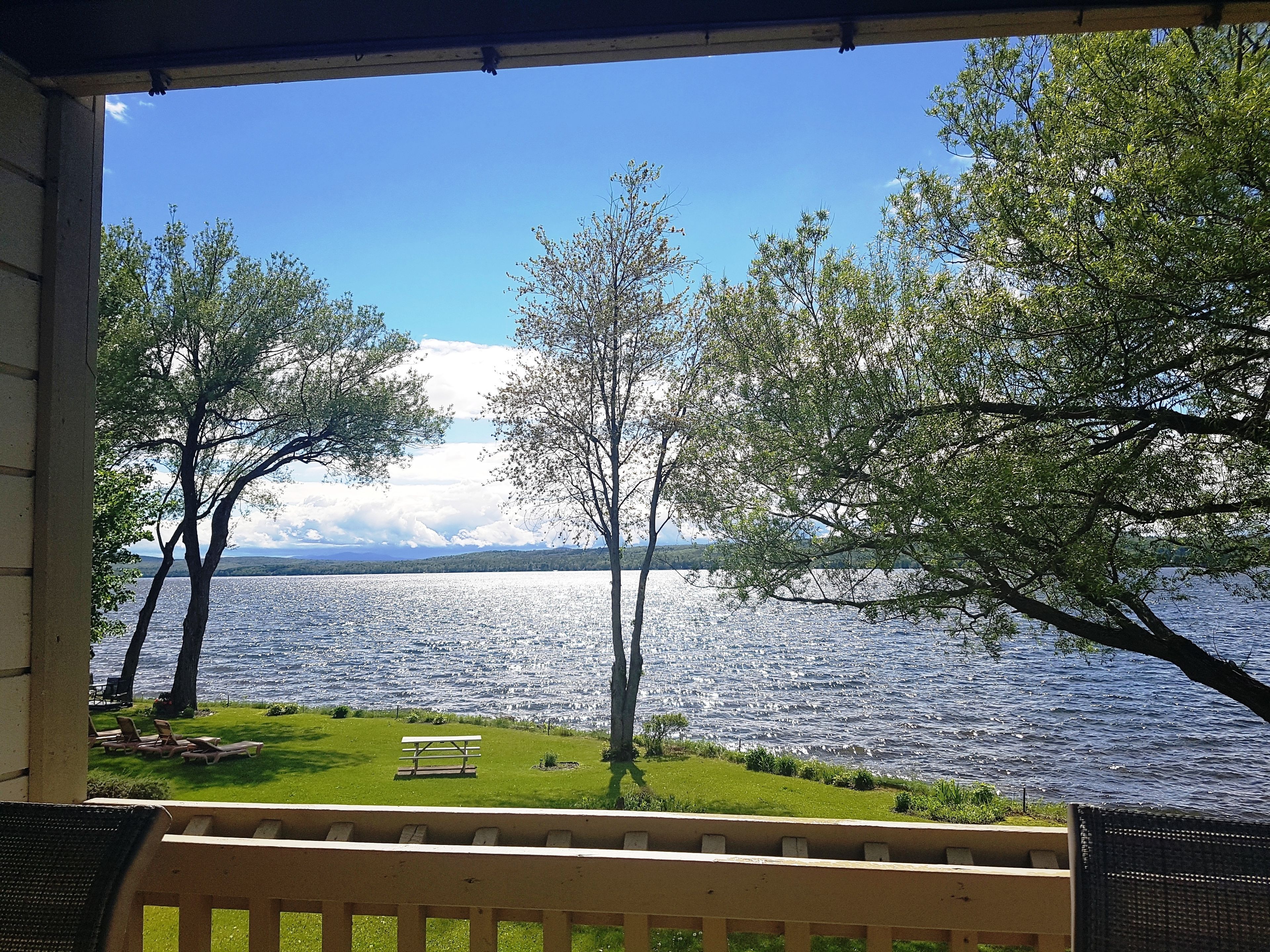 A view from a covered porch overlooking a lake with trees and a bench.