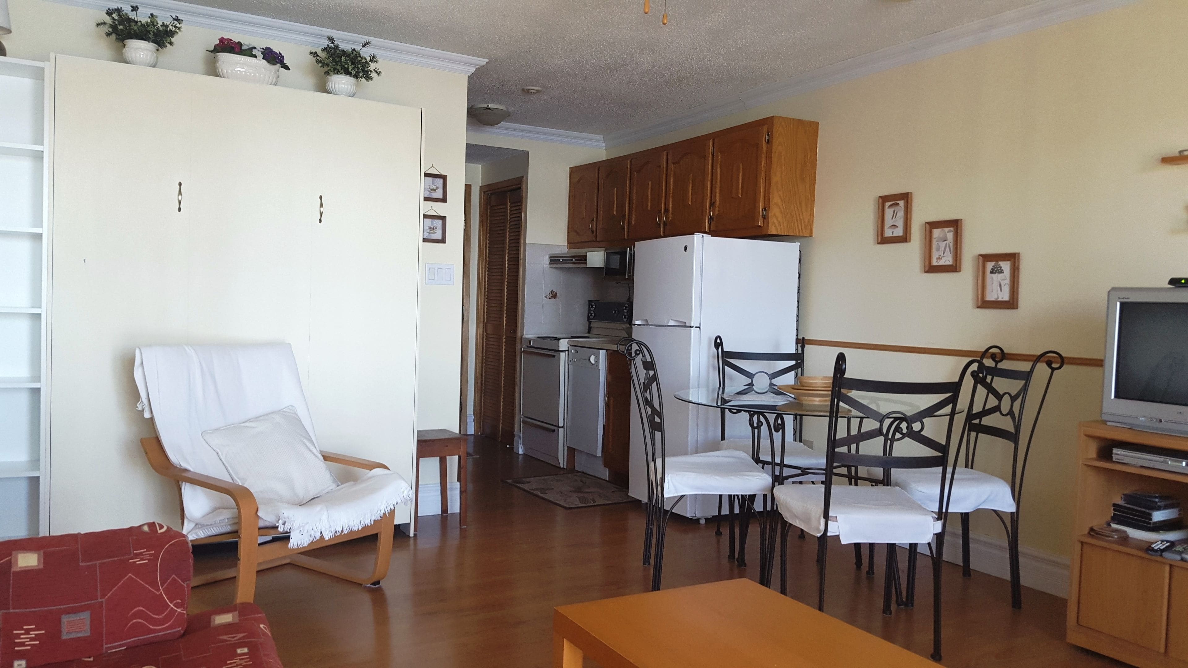 Un espacio habitable compacto con comedor, cocina equipada con refrigerador y estufa, y televisor sobre un soporte de madera.