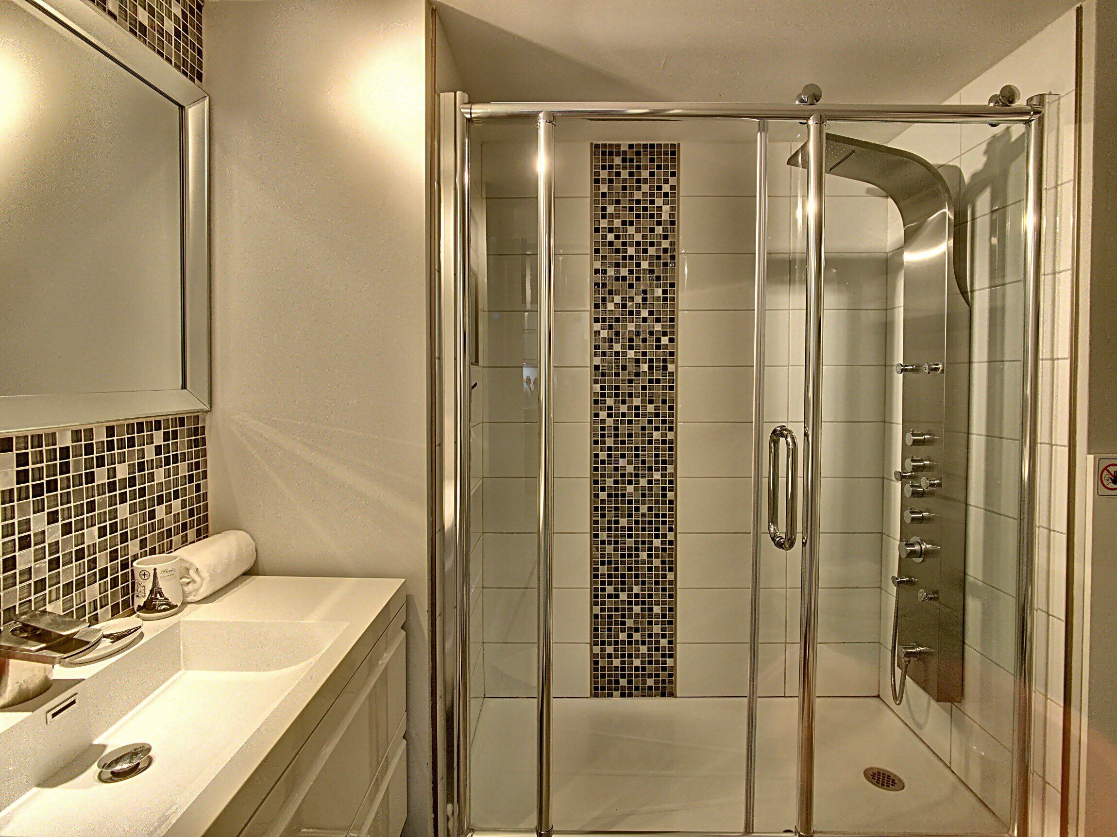 Un bagno moderno con doccia vetrata, lavandino bianco con specchio e schienale piastrellato.