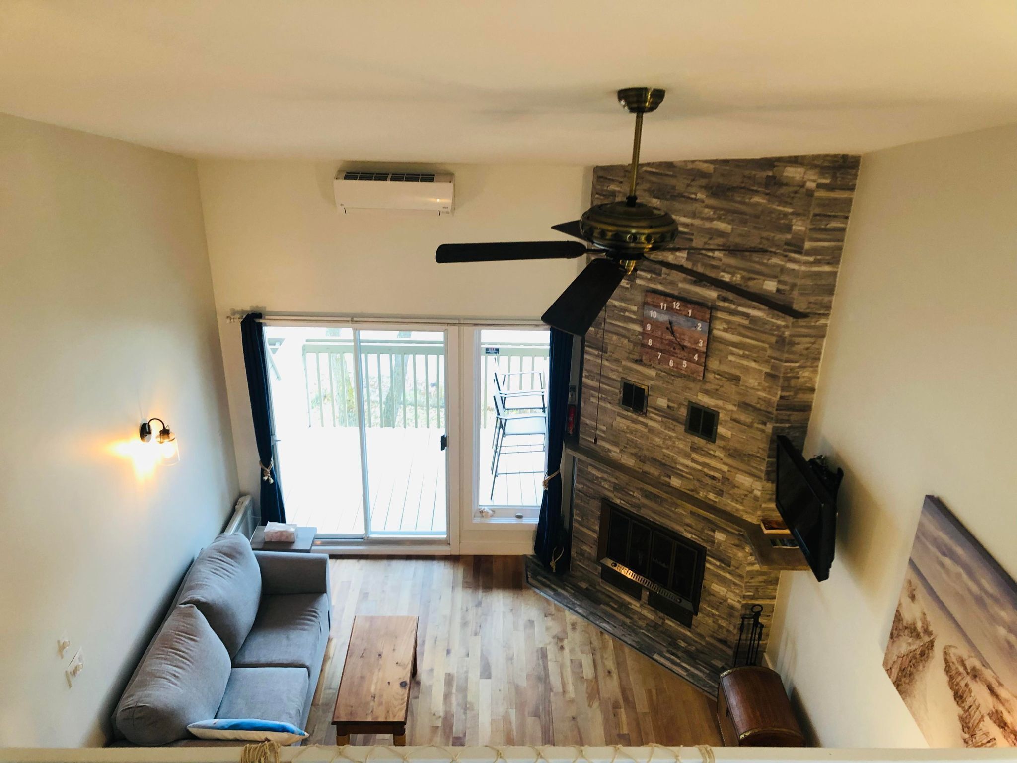 Un salon doté d’une cheminée en pierre, d’un ventilateur de plafond, d’un canapé et d’une porte-fenêtre coulissante donnant sur une terrasse extérieure.