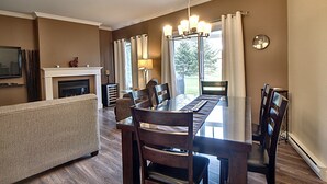 A dining area with a wooden table and chairs, a fireplace, and a view of the outdoors. - Condo 2 Bedrooms Jardin des Sables (Orford)