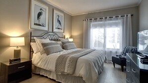 A neatly arranged bedroom with a bed, bedside tables, a dresser, and a television. - Condo 2 Bedrooms Jardin des Sables (Orford)