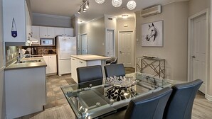 A modern kitchen with white cabinets, a refrigerator, and a dining area with a glass table and chairs. - Condo 2 Bedrooms Jardin des Sables (Orford)