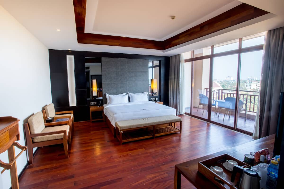 Ein modernes Hotelzimmer mit einem großen Bett, Holzboden, einem Balkon mit Sitzgelegenheiten und einem Essbereich mit einem Tablett mit Frühstücksartikeln.