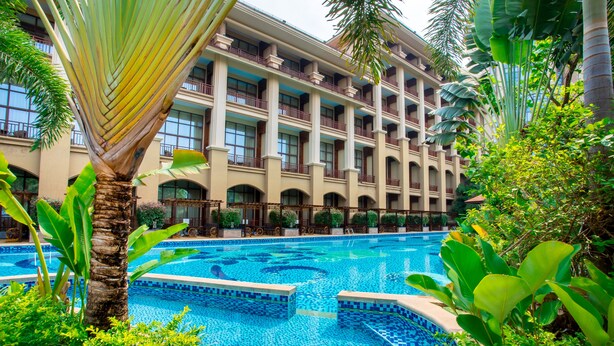 Un hôtel doté d’une grande piscine, entourée d’une végétation luxuriante et de palmiers.