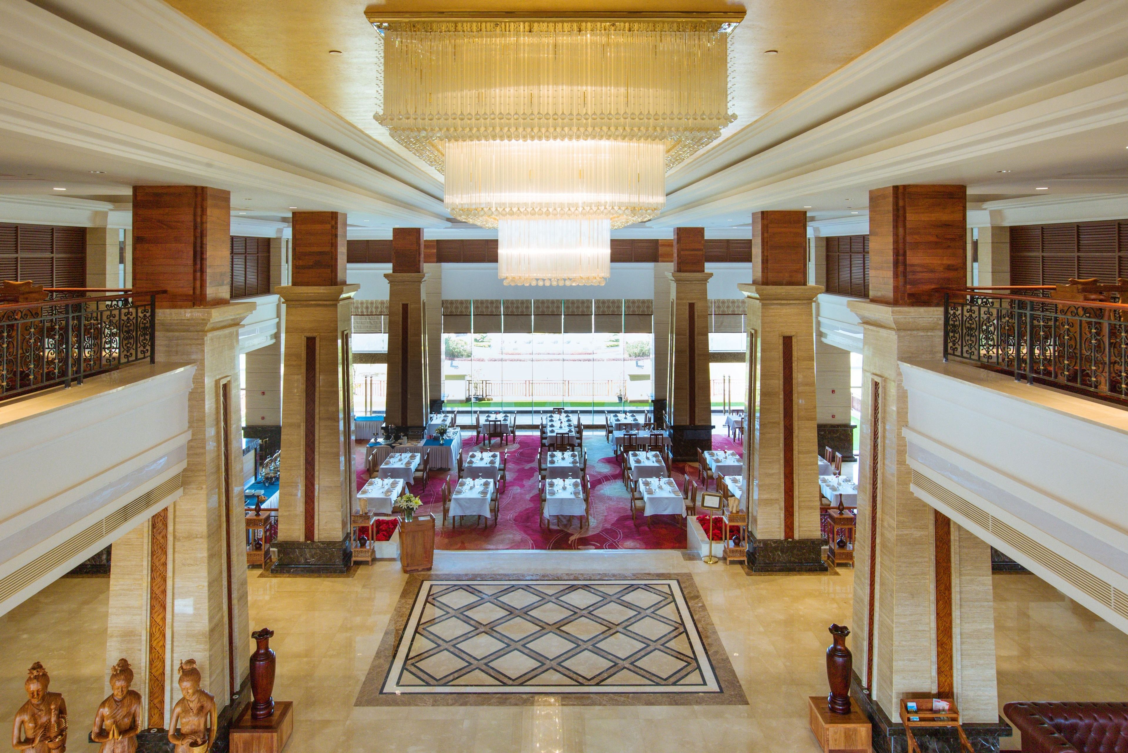 Eine geräumige Lobby mit einem prächtigen Kronleuchter, mehreren Essbereichen und klassischen architektonischen Elementen wie Säulen und Geländern.