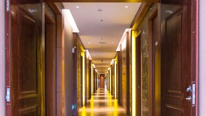 Un long couloir étroit, avec des portes en bois de chaque côté, qui mène à une pièce lumineuse et bien éclairée au bout.