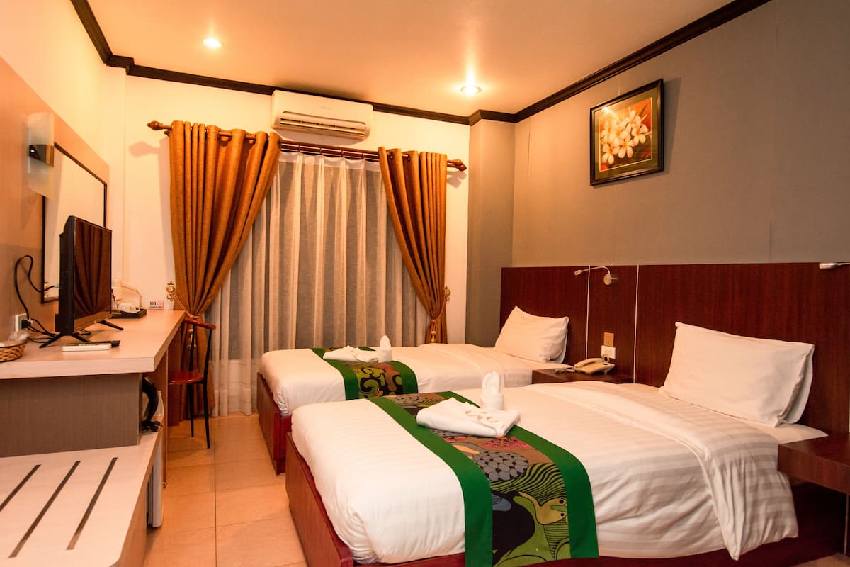 Quarto de hotel com duas camas, uma escrivaninha, uma cadeira, aparelho de ar condicionado e um quadro na parede.