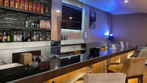 Un espace bar avec des étagères remplies de bouteilles d’alcool, un comptoir avec des verres et un tableau affichant le menu.