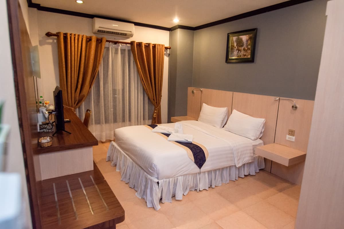 Quarto de hotel com cama grande, escrivaninha com cadeira, mesa de cabeceira pequena e TV fixada na parede.