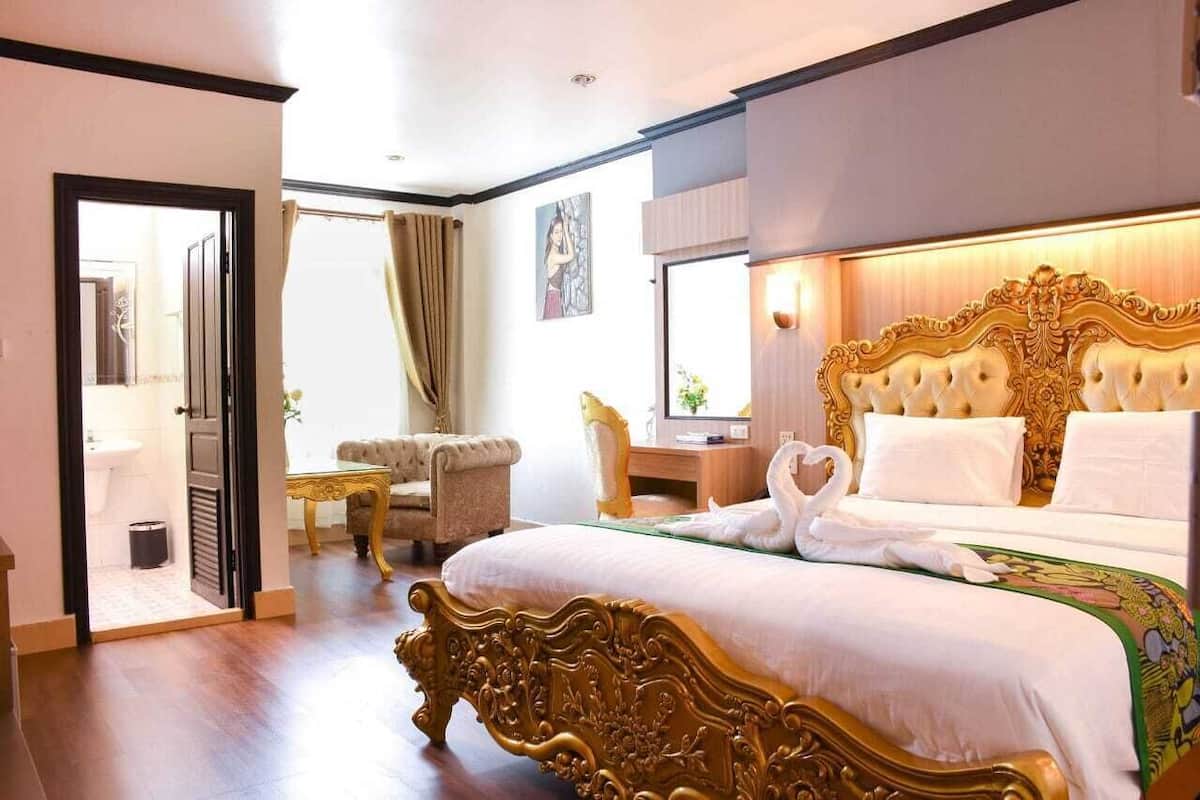 Quarto de hotel com uma cama grande, uma escrivaninha, uma cadeira e um banheiro visível através de uma porta aberta.
