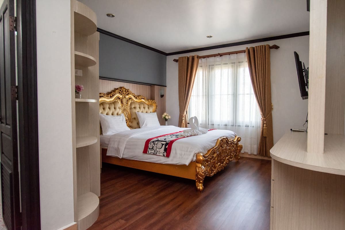 Um quarto espaçoso com cama grande, estantes embutidas, TV de tela plana e janela com cortinas.