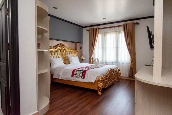 A spacious bedroom with a large bed, built-in shelving, a flat-screen TV, and a window with curtains.