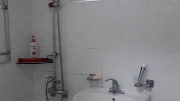 A bathroom with a white sink, a toilet, a shower with a red handle, and a window above the sink.