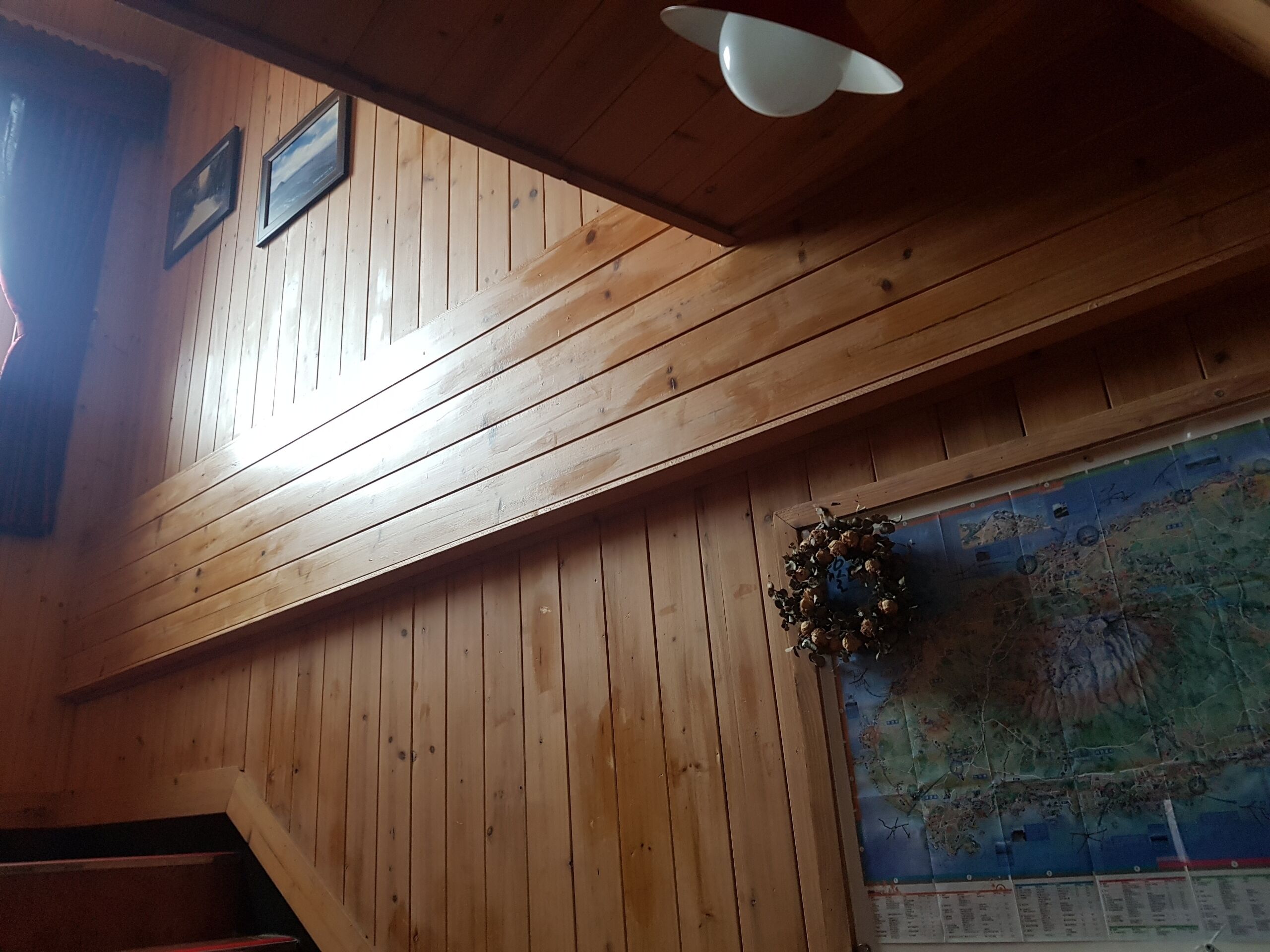 Un interior de madera con techo inclinado, un mapa en la pared y una decoración con corona de laurel.