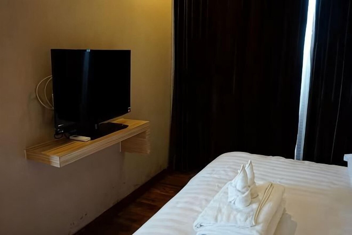 A hotel room with a bed, a TV on a wooden shelf, and a window with curtains.