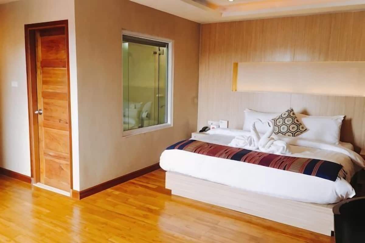Une chambre avec un plancher en bois, un lit recouvert d’une couverture à rayures, une table de chevet avec une lampe et une fenêtre donnant sur un beau paysage.