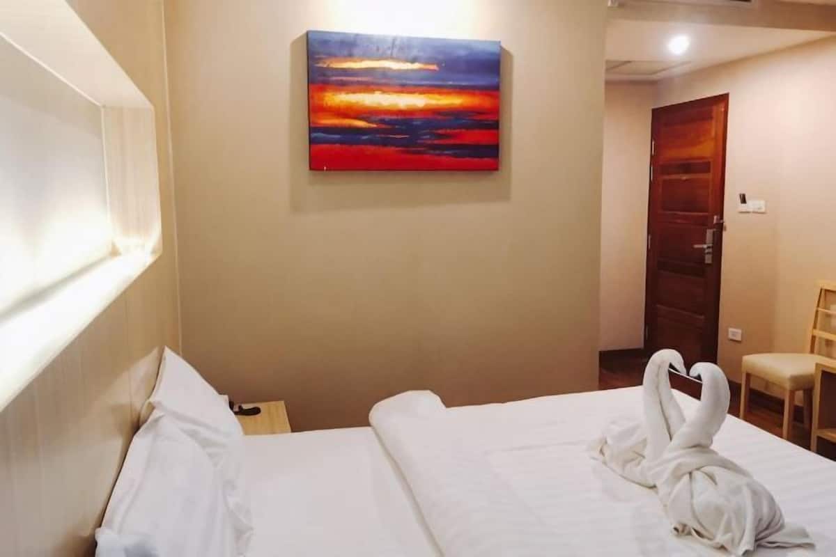 Une chambre d’hôtel avec un lit, un tableau représentant un coucher de soleil et une chaise.