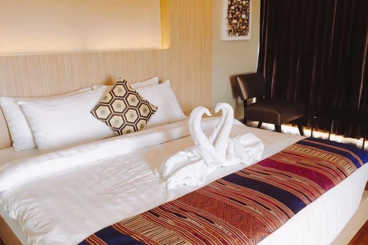 A neatly made bed with white linens, a decorative pillow, and two white swan-shaped towels.