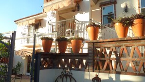 A building with a balcony, potted plants, and a decorative metal clock.