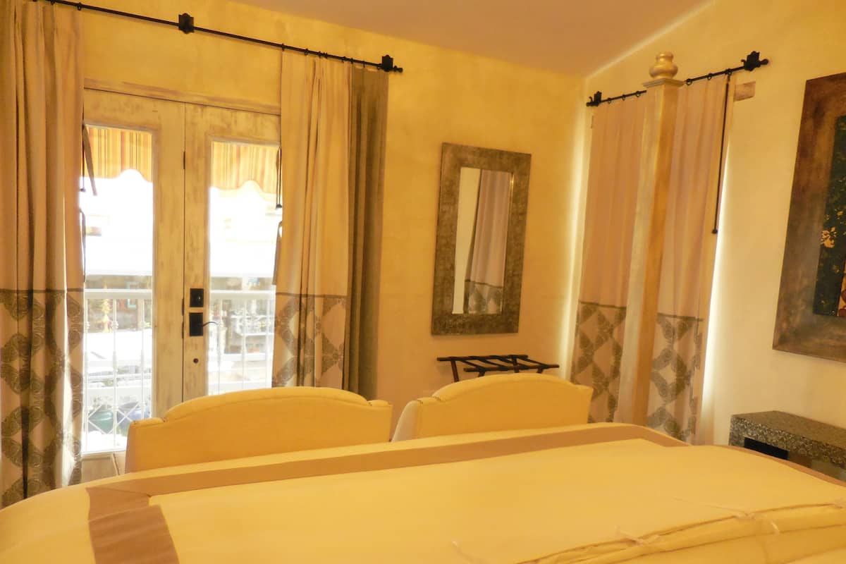Een hotelkamer met een bed, twee stoelen, een tafeltje, een spiegel en een balkon met gordijnen.