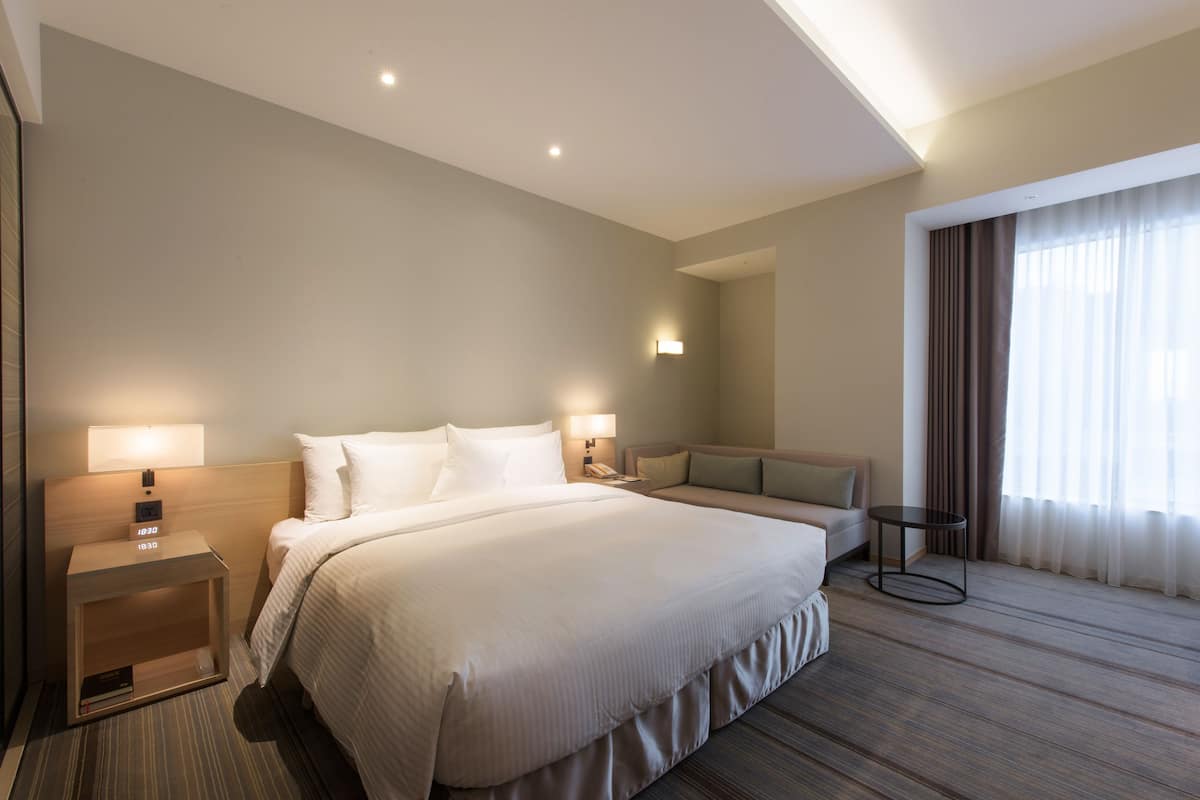 Une chambre d’hôtel moderne avec un grand lit, des tables de chevet, un canapé et une petite table.