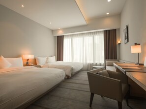 A hotel room with two beds, a desk, a chair, a small round table, and a window with curtains.