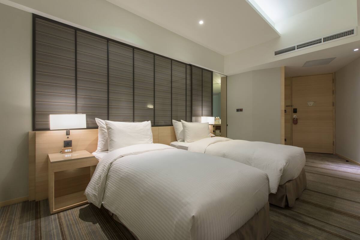 Une chambre d’hôtel avec deux lits, un grand miroir, une table de chevet avec une lampe et une porte en bois.