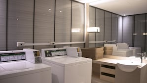 A modern hotel bathroom with a large mirror, a washing machine, a sink, and a basket of towels. - HOTEL COZZI Zhongshan Kaohsiung (Kaohsiung)