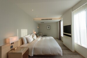 A hotel room with a large bed, bedside tables, a TV, and a window with curtains.