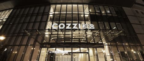Un edificio moderno con fachada de vidrio y señalización iluminada que dice "COZZI".