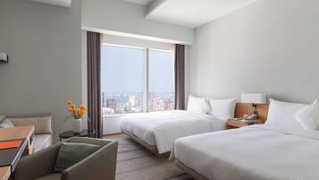 Habitación de hotel con dos camas, un escritorio, una silla y vista a la ciudad.