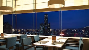 A restaurant with tables and chairs, large windows with a cityscape view, and hanging lamps. - HOTEL COZZI Zhongshan Kaohsiung (Kaohsiung)