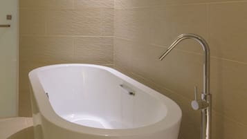 A modern bathroom with a freestanding bathtub, a wall-mounted faucet, and beige tiled walls.