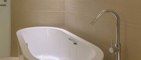 A modern bathroom with a freestanding bathtub, a wall-mounted faucet, and beige tiled walls.