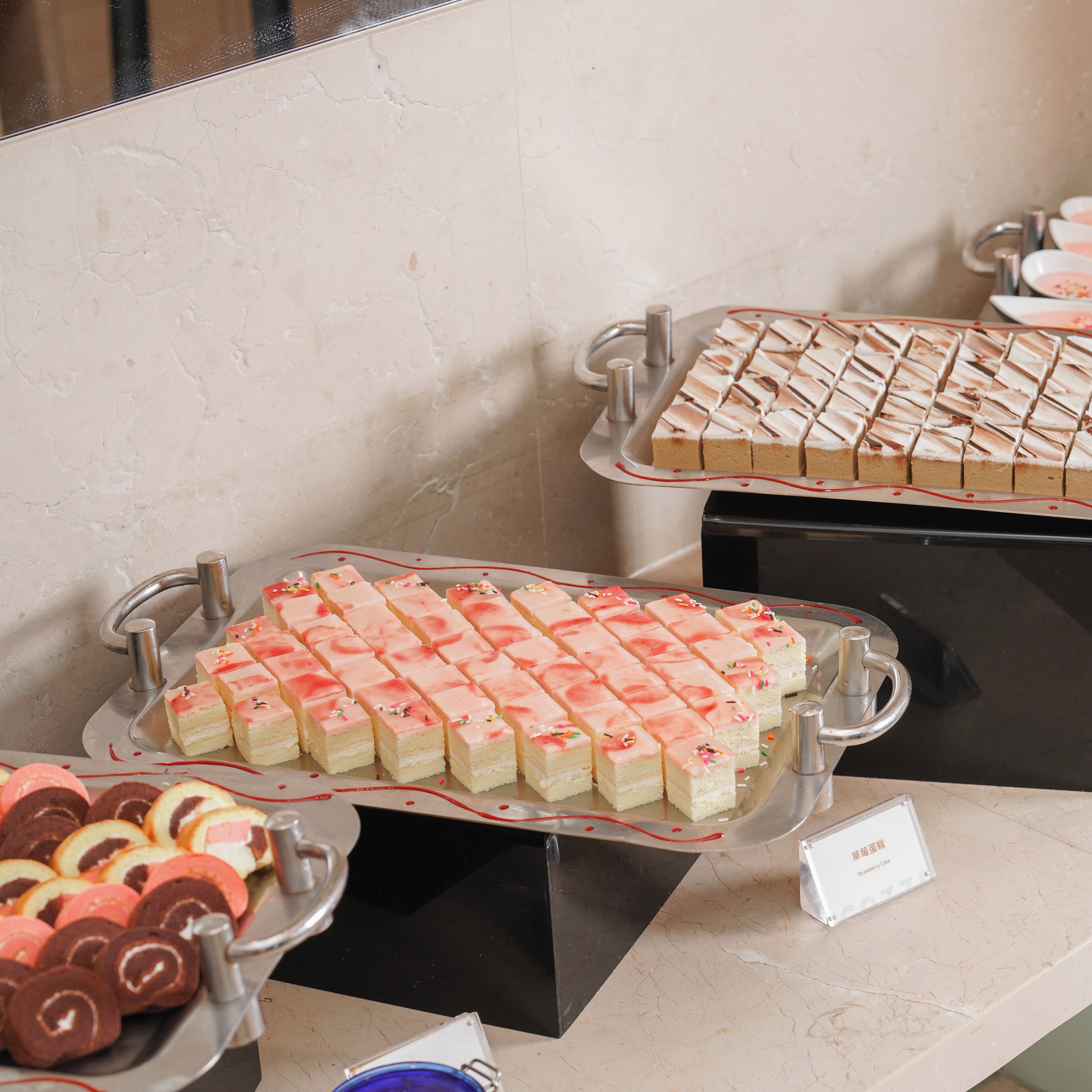 A buffet with various desserts, including pink and white frosted cakes, and chocolate rolls.