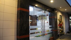 A hotel entrance with a glass facade, a red stripe, and a floral decoration. - KL Hotel (Labuan)