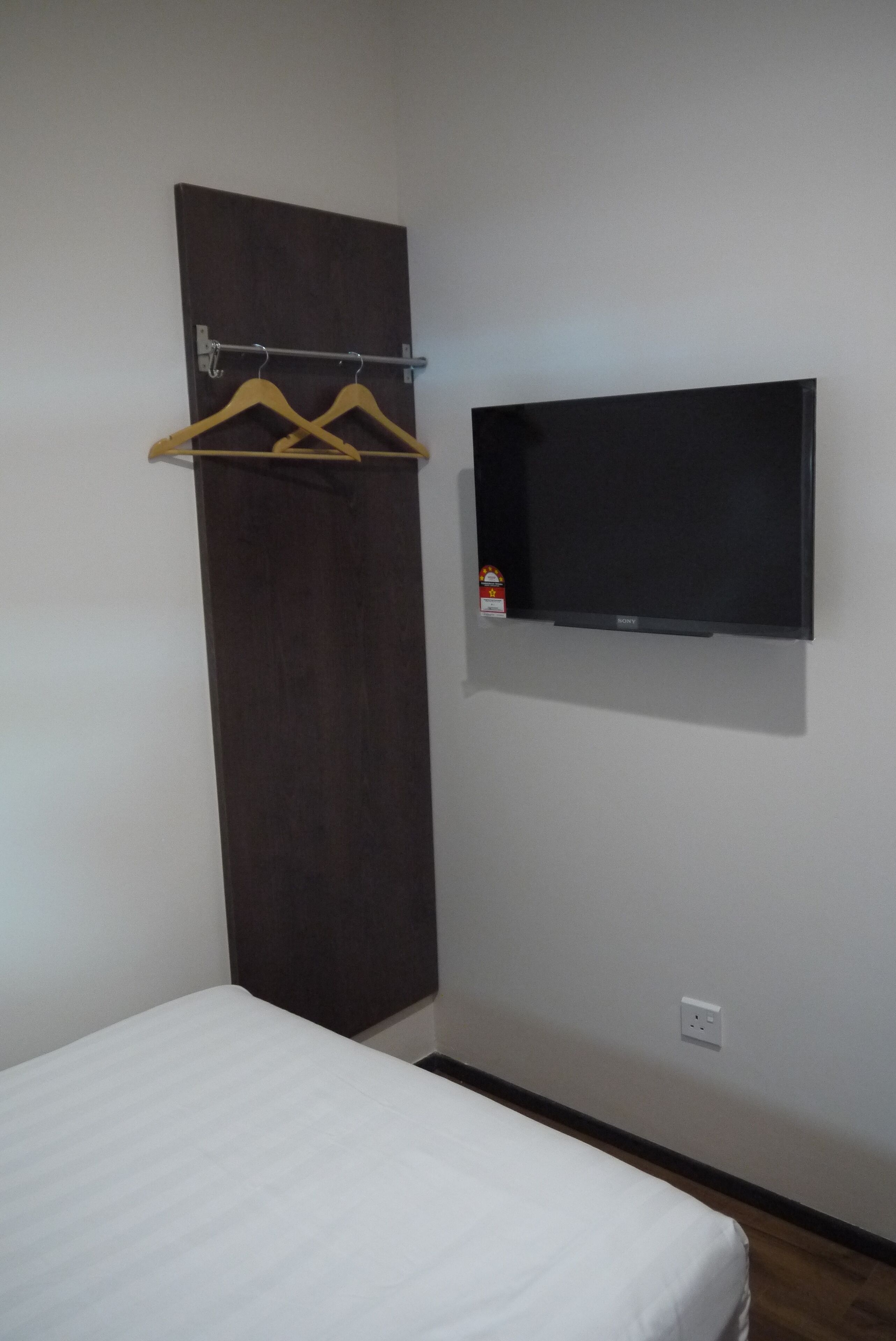 A room with a bed, a dark wooden wardrobe, a wall-mounted TV, and a clothes hanger.