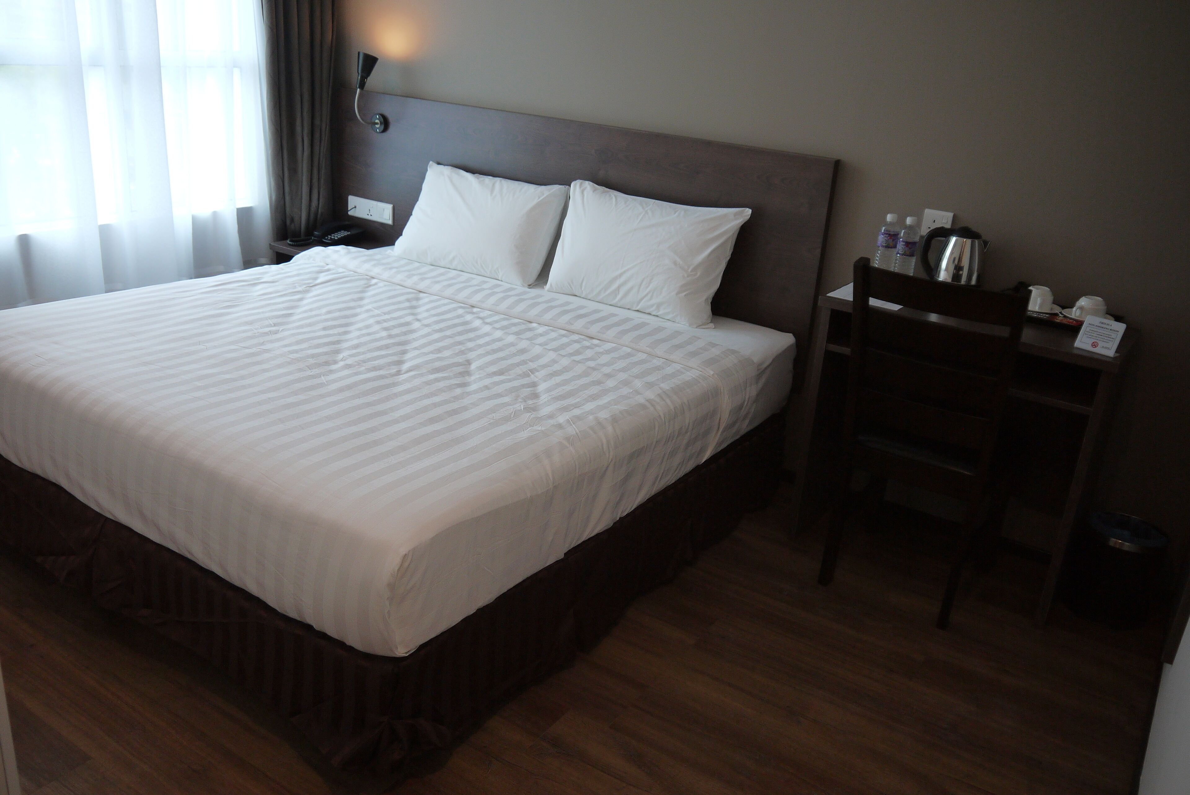 A neatly made bed with white linens, a wooden headboard, a bedside table with a lamp, and a chair.