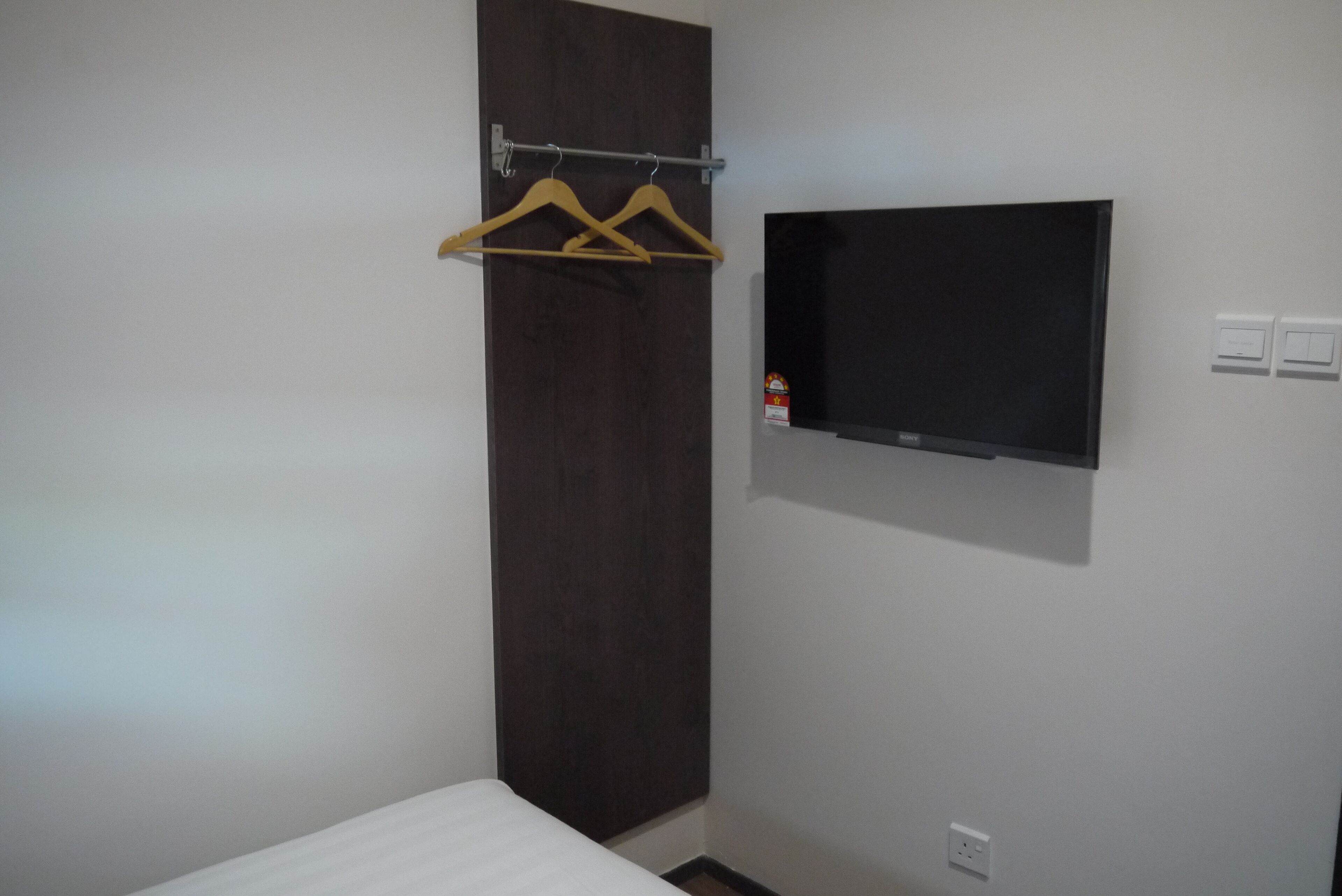 Una habitación con cama, un armario de madera oscura, un televisor montado en la pared y un perchero.