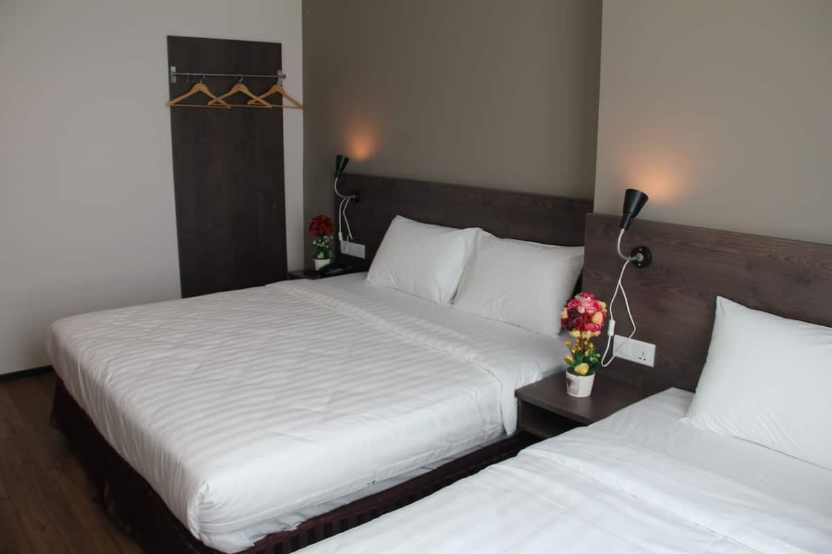 Habitación de hotel con dos camas, cabeceros de madera, mesitas de noche con lámparas y una pequeña planta en maceta.