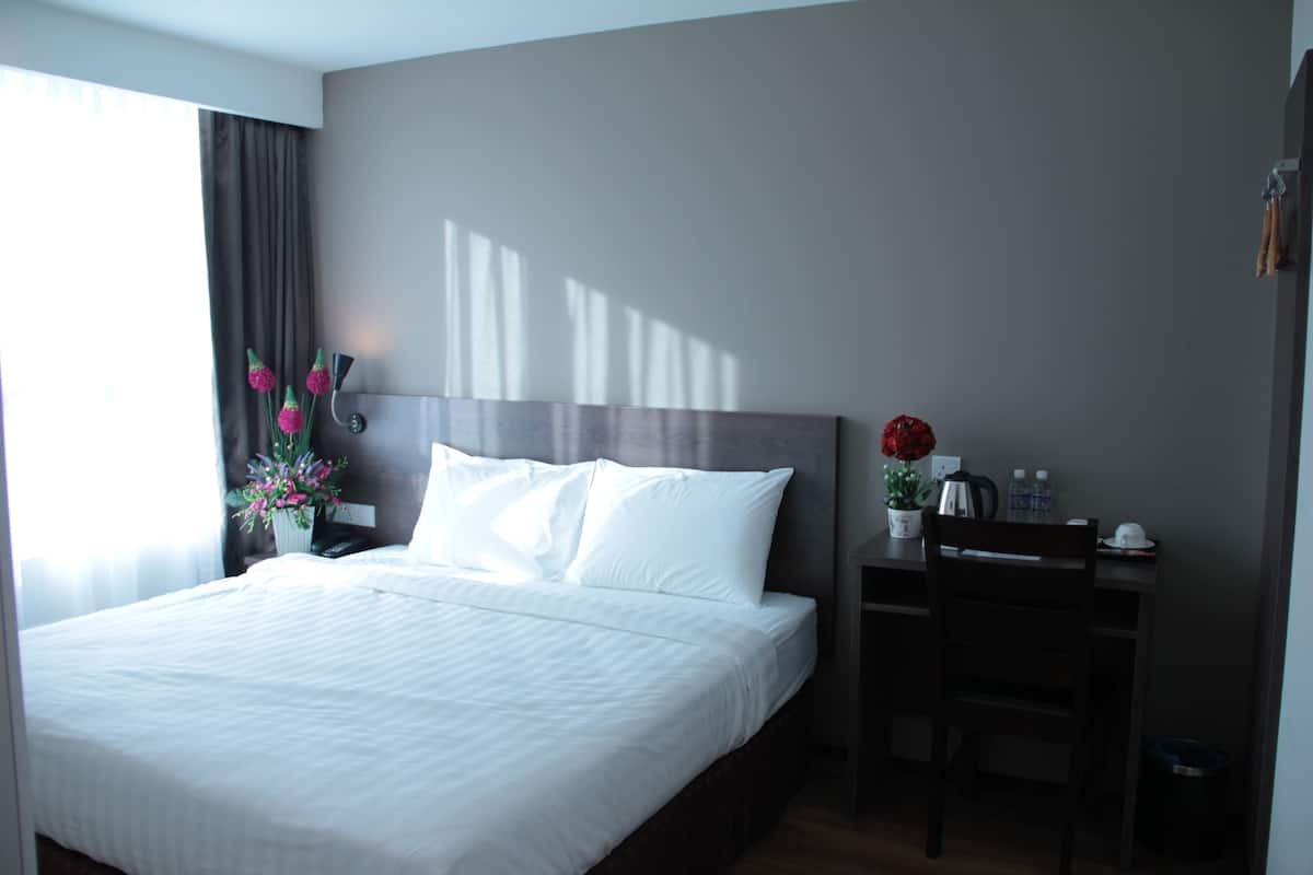 Habitación de hotel con una cama grande, un escritorio y una silla. Hay una ventana con cortinas y un florero sobre el escritorio.