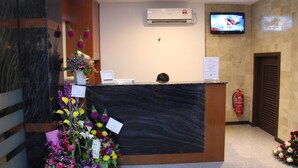 A reception desk with a flat-screen TV above it, a fire extinguisher on the wall, and a bouquet of flowers on the left. - KL Hotel (Labuan)