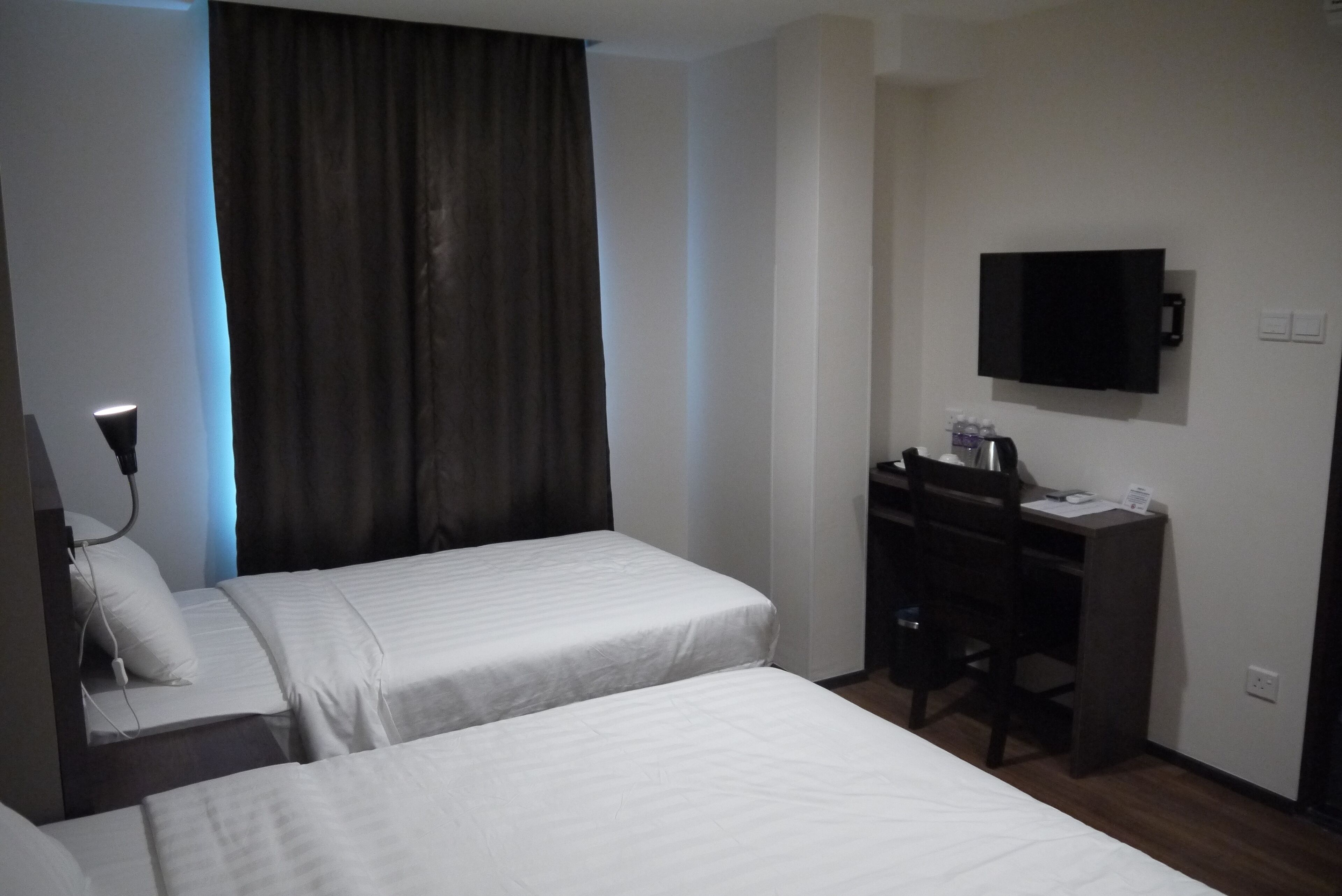 Een hotelkamer met twee bedden, een bureau, een stoel, een aan de muur bevestigde televisie en een gordijn.