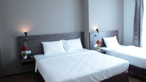 A hotel room with two single beds, a bedside table with a lamp, and a nightstand with a phone and a vase of flowers. - KL Hotel (Labuan)