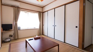 Una habitación con suelo de tatami, una mesa de madera baja, un televisor sobre una estantería, puertas correderas y una lámpara en el techo.