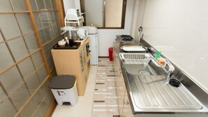 Cocina compacta con lavabo, estufa y microondas. Hay un cubo de basura pequeño y un taburete.